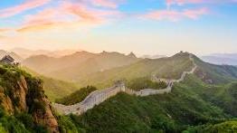 Sunset view of the Great Wall of China winding over surrounding mountains.