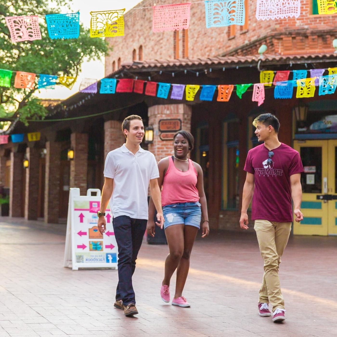 three Trinity students walk through Market Square under papel picado