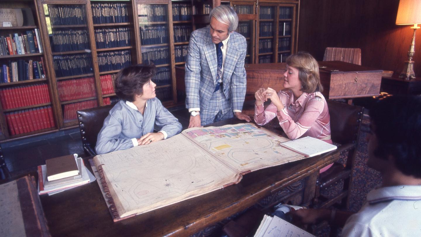 一个男人站着和两个女人聊天，同时看着赌博娱乐平台网址大全的校园地图.