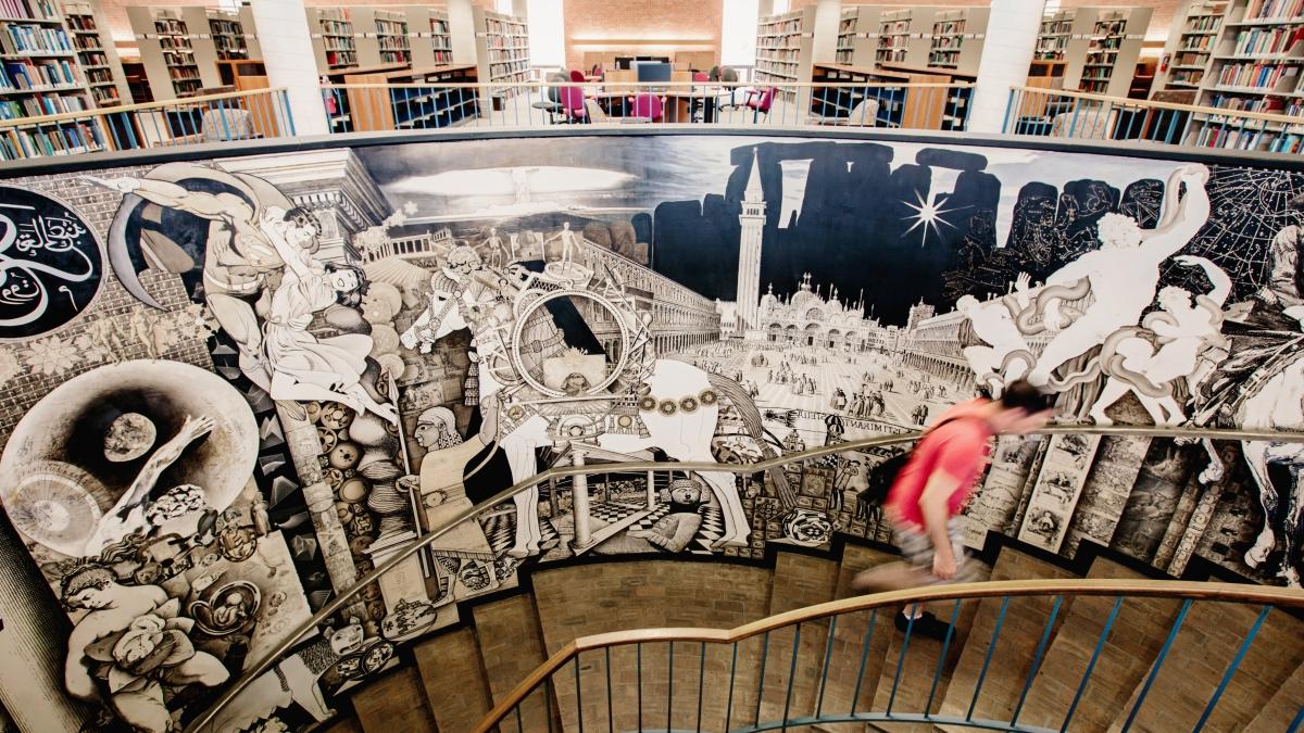 Student climbs spiral stairwell decorated with a mural in Coates Library