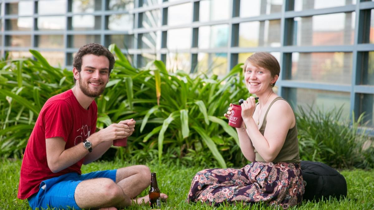 two students sit in the grass eating ice cream from maroon cups